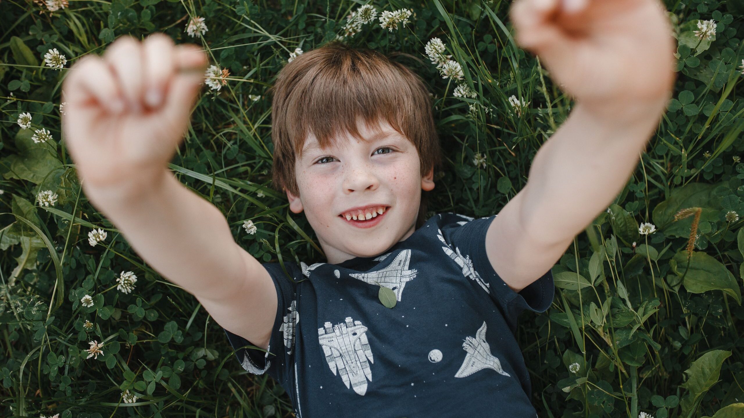 A happy child lying in a garden with arms raised, surrounded by flowers and greenery.