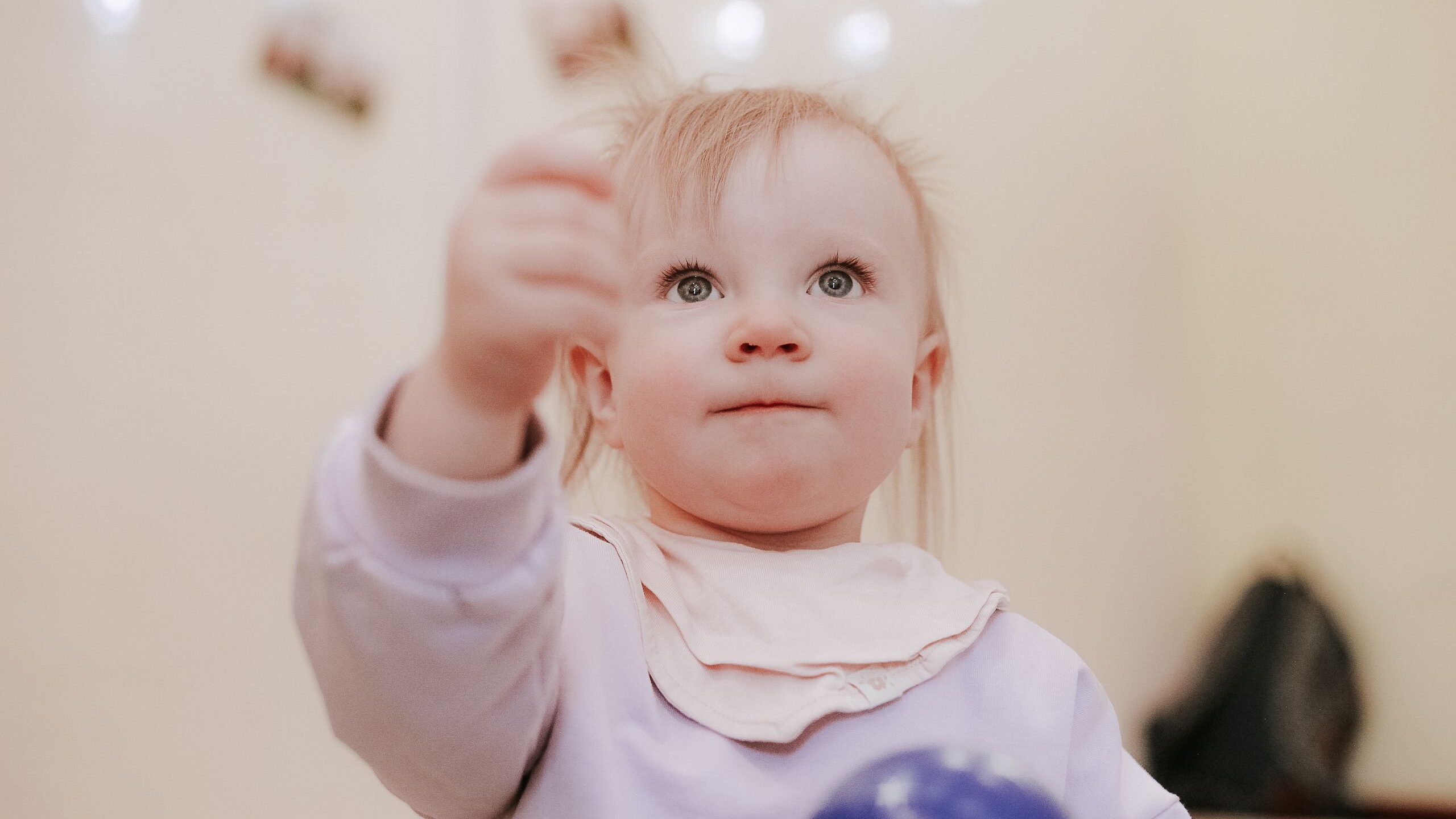 Charming toddler in a long sleeve shirt playing with a blue ball indoors.
